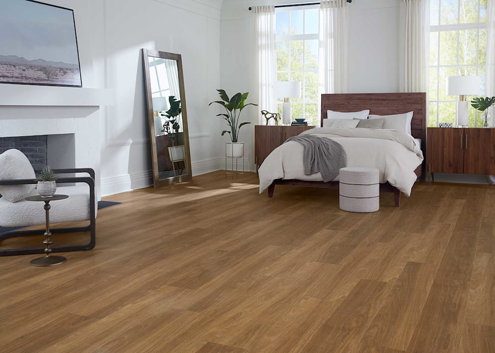 8mm with Pad Mission Beach Oak Waterproof Rigid Vinyl Plank Flooring in bedroom with bed with dark brown wood headboard and off white bedding plus floor mirror and white plaster fireplace