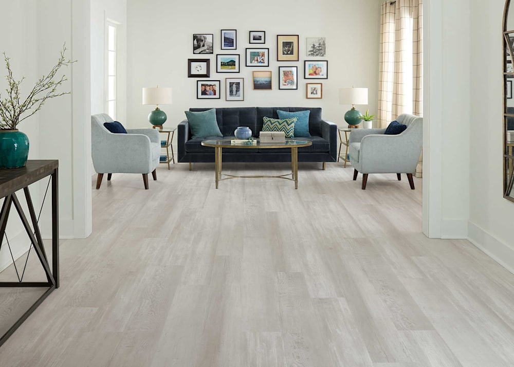 6mm with Pad New Pearl Cove Rigid Vinyl Plank Flooring in living room with dark blue upholstered sofa and pale blue accent chairs plus art gallery wall