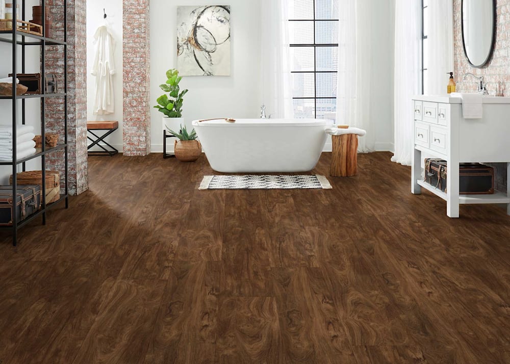 8mm with Pad Antique Brazilian Cherry Waterproof Rigid Vinyl Plank Flooring in bathroom with freestanding white bathtub and white oversized vanity plus exposed brick beams and black glass shelving