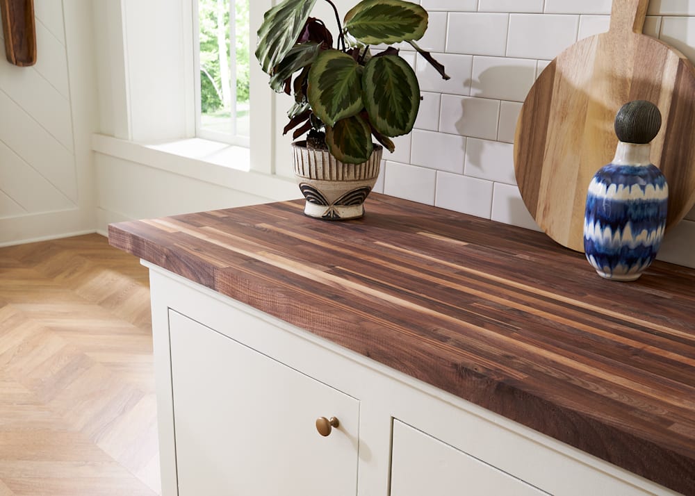 Unfinished Signature American Walnut Butcher Block Countertop 12 ft. L x 25 in. W x 1-1/2 in. Th on countertop in kitchen with subway tile on wall and round cutting board against wall