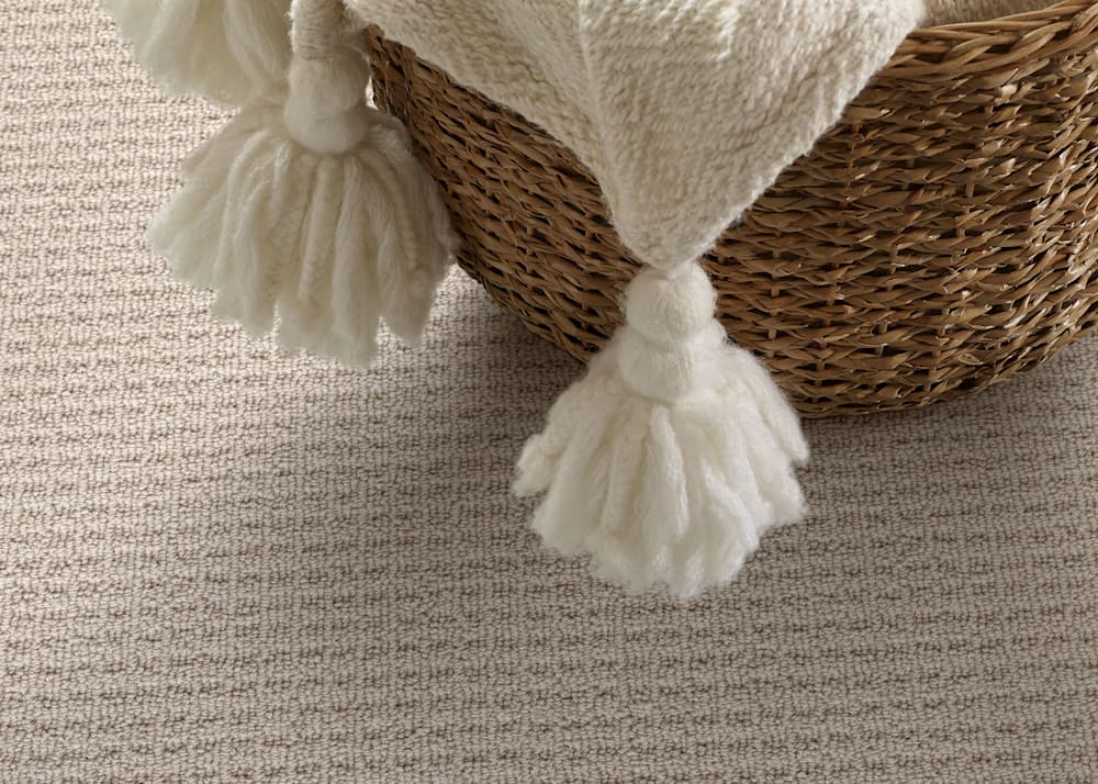 Carrington Cove Carpet in Cashmere close up of carpet and rattan basket with off white blanket