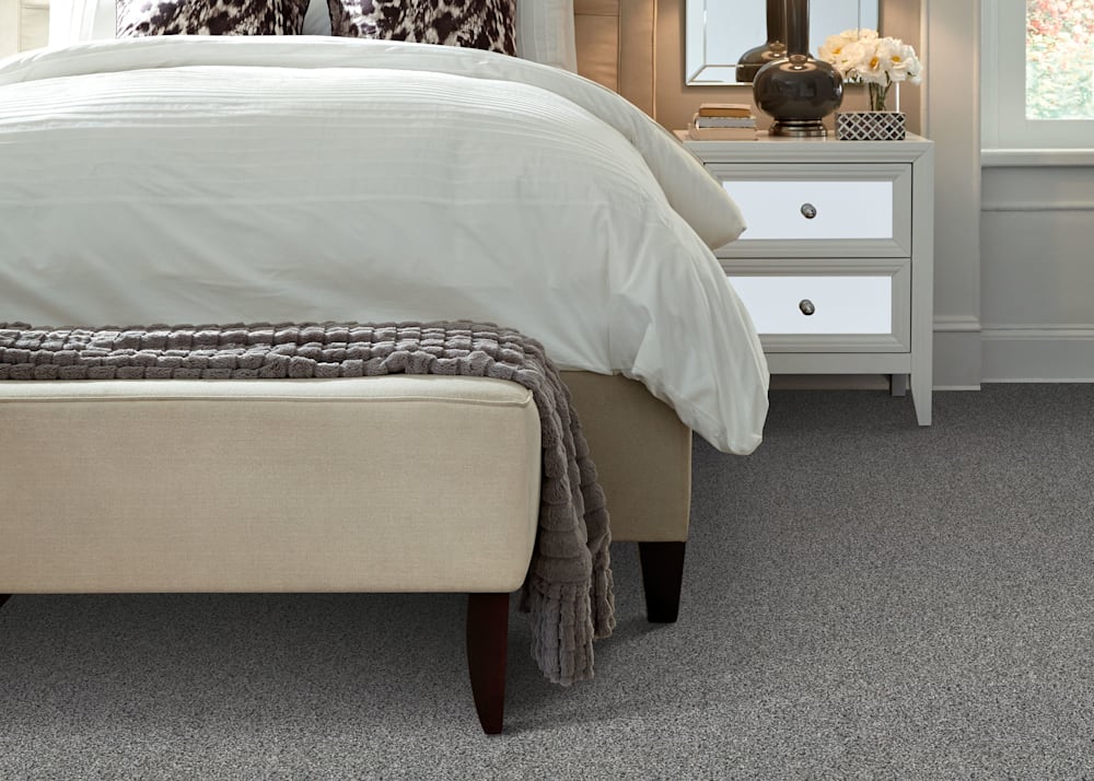 New Rochelle Carpet in Storm in bedroom with taupe upholstered bed with off white bedding and cream upholstered bench and mirrored side table